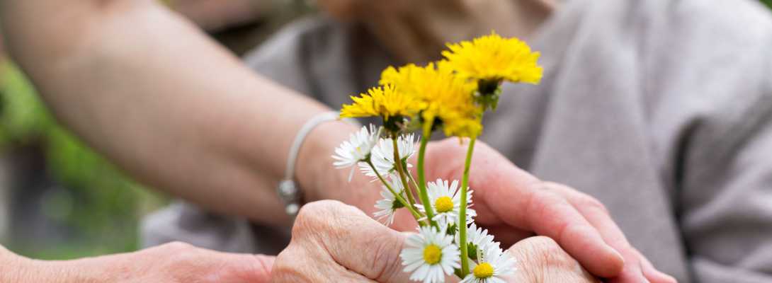 Un'anziana tiene dei fiori in mano, una donna la aiuta